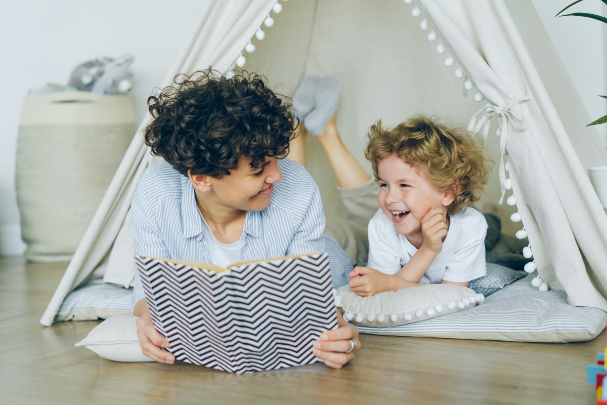 A parent and laughing child reading together in a play tent